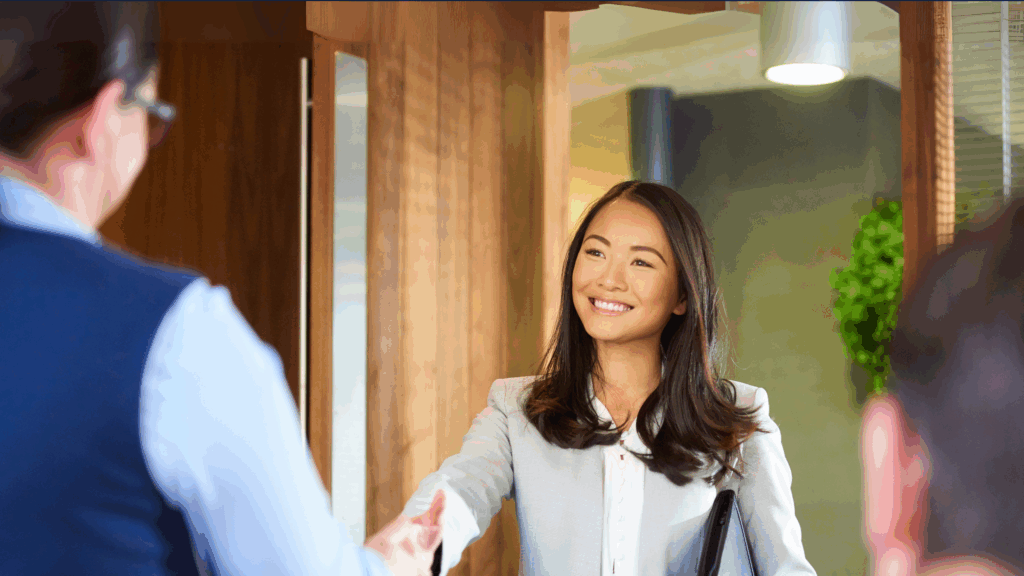 Smiling female hospitality leader greeting a colleague with a handshake in a modern office, symbolizing female leadership in hospitality and operational real estate.